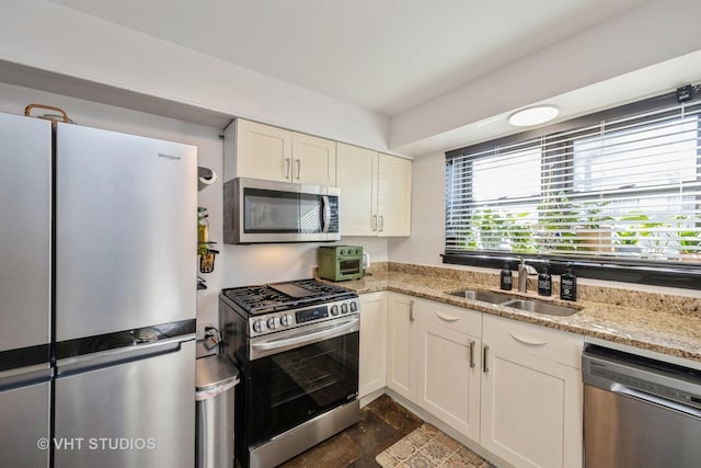 kitchen with light stone countertops, a toaster, a sink, stainless steel appliances, and white cabinetry