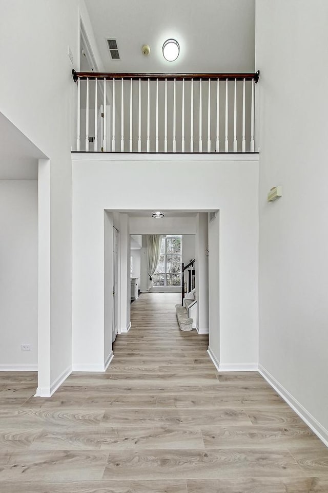 interior space with visible vents, a towering ceiling, baseboards, and wood finished floors