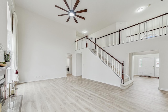 unfurnished living room with stairway, a towering ceiling, light wood-style floors, washer / dryer, and baseboards