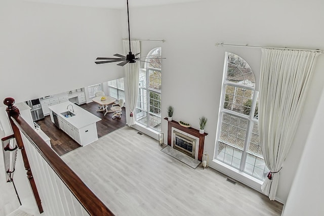 living room featuring visible vents, a glass covered fireplace, ceiling fan, wood finished floors, and a high ceiling