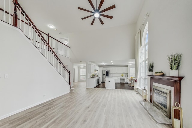 living room featuring light wood finished floors, a tile fireplace, a towering ceiling, and a healthy amount of sunlight