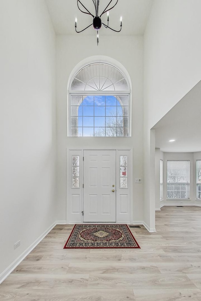 entryway with a chandelier, a wealth of natural light, a towering ceiling, and wood finished floors