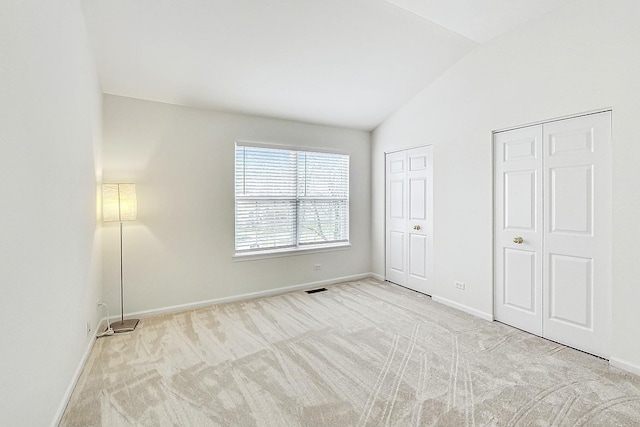 unfurnished bedroom featuring lofted ceiling, carpet flooring, visible vents, baseboards, and multiple closets