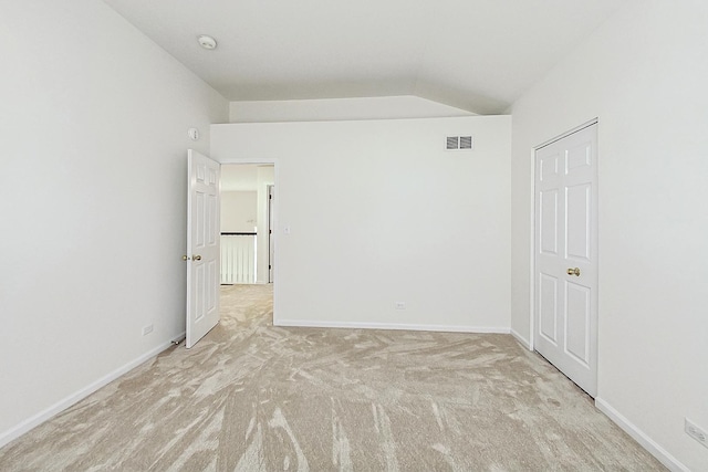 carpeted empty room featuring visible vents, vaulted ceiling, and baseboards