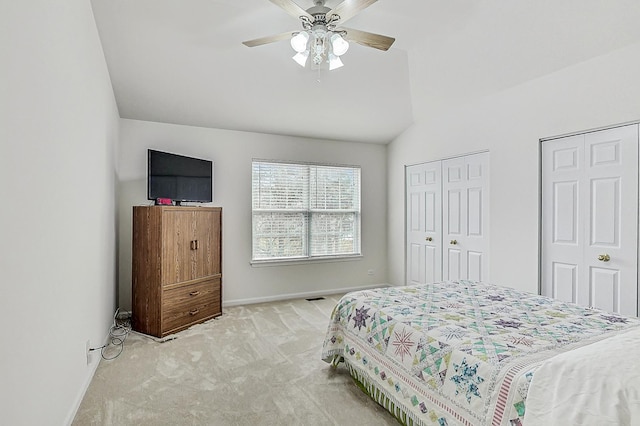 carpeted bedroom with lofted ceiling, a ceiling fan, visible vents, baseboards, and two closets