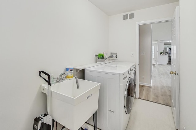 laundry area with laundry area, light wood finished floors, visible vents, washing machine and dryer, and a sink