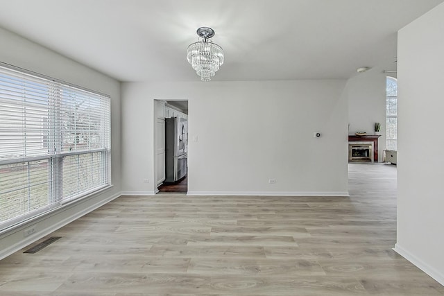 unfurnished room featuring visible vents, a notable chandelier, light wood-style flooring, and baseboards