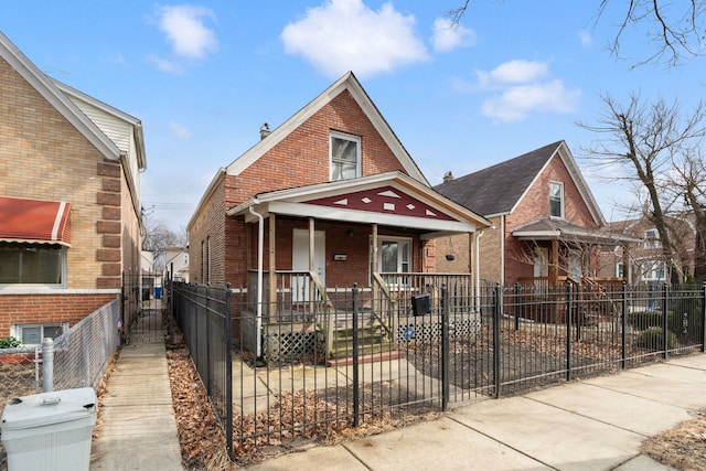 bungalow featuring covered porch, brick siding, and a fenced front yard