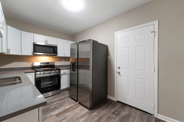 kitchen with stainless steel appliances, white cabinetry, baseboards, light wood-type flooring, and dark stone countertops