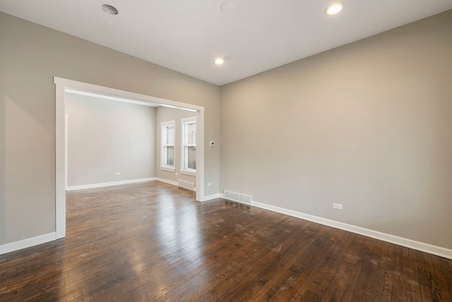 spare room with dark wood-type flooring, visible vents, and baseboards