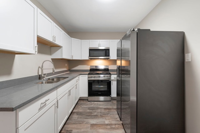 kitchen with stainless steel appliances, dark countertops, white cabinets, a sink, and wood finished floors