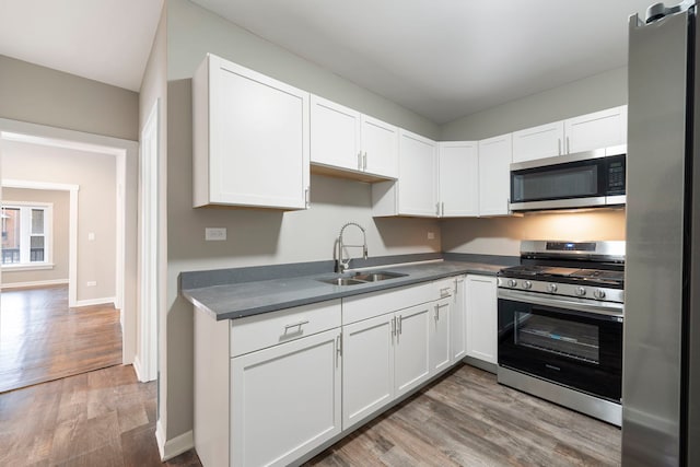 kitchen featuring white cabinets, stainless steel appliances, a sink, and wood finished floors