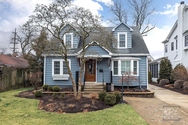 new england style home with a shingled roof, fence, and a front lawn