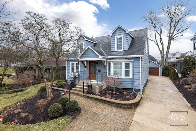 new england style home with a shingled roof, an outbuilding, and a garage