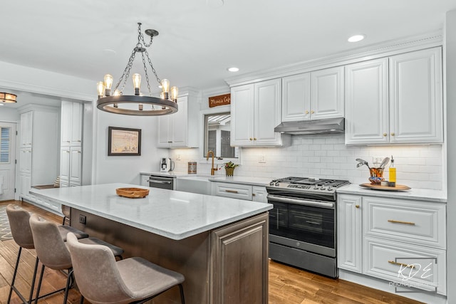 kitchen with appliances with stainless steel finishes, white cabinetry, a sink, a kitchen island, and under cabinet range hood