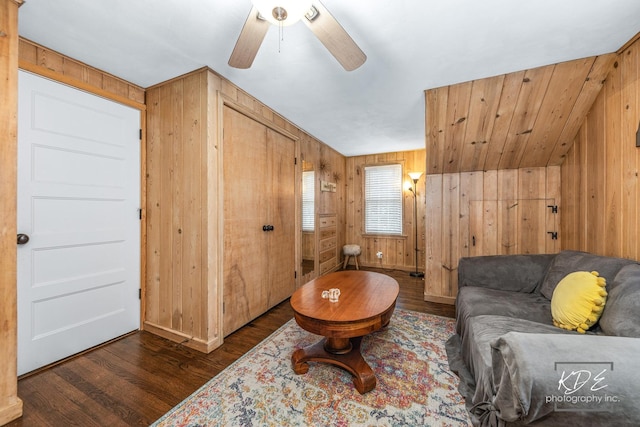 living room with wooden walls, a ceiling fan, and dark wood-type flooring