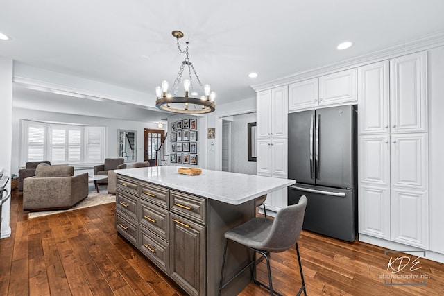 kitchen featuring a breakfast bar area, open floor plan, dark wood-type flooring, freestanding refrigerator, and white cabinetry