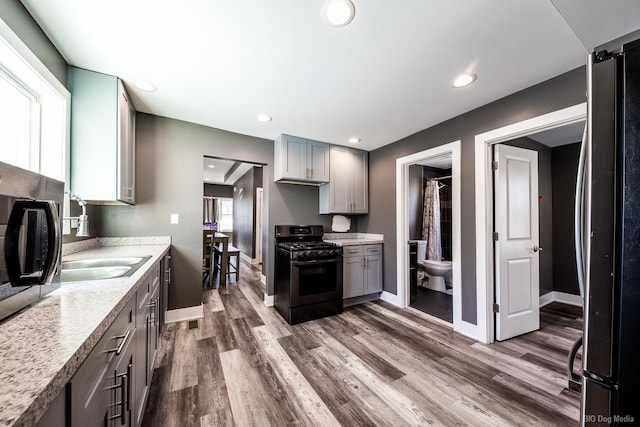 kitchen featuring black range with gas cooktop, dark wood-style flooring, gray cabinets, and freestanding refrigerator