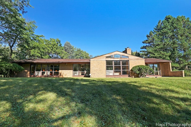 back of property featuring a yard, brick siding, and a chimney