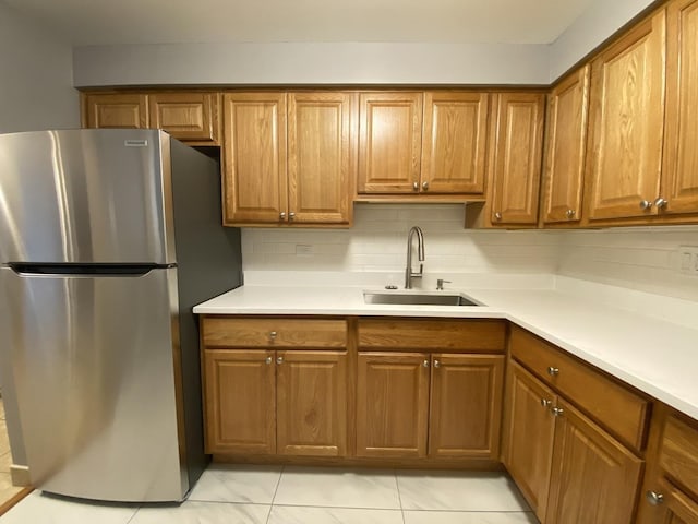 kitchen featuring brown cabinetry, a sink, and freestanding refrigerator