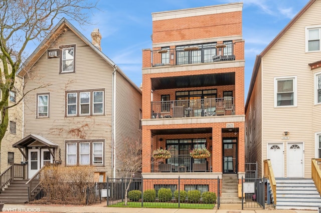 view of front facade featuring brick siding, a balcony, and a fenced front yard