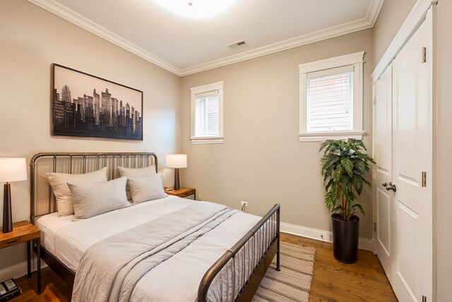 bedroom with visible vents, ornamental molding, baseboards, and wood finished floors