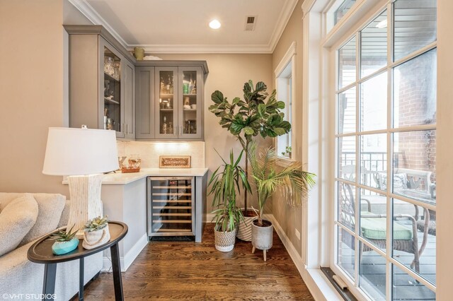 bar with beverage cooler, dark wood-style flooring, a bar, crown molding, and tasteful backsplash