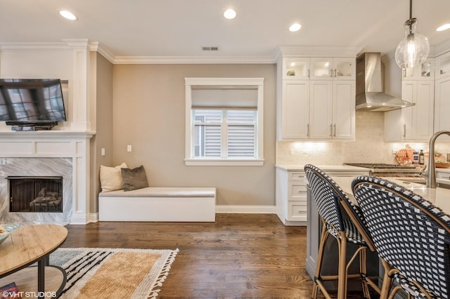 kitchen featuring dark wood-type flooring, wall chimney exhaust hood, crown molding, and hanging light fixtures