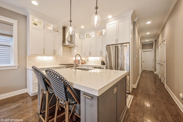 kitchen featuring an island with sink, ornamental molding, a sink, wall chimney exhaust hood, and backsplash