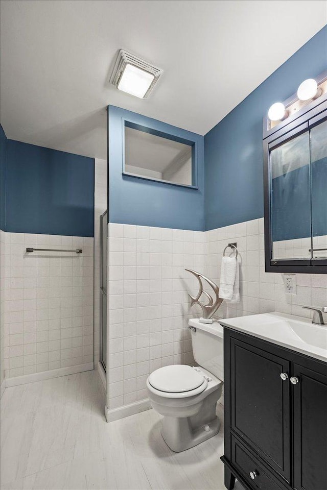 bathroom with a walk in shower, toilet, visible vents, vanity, and tile walls