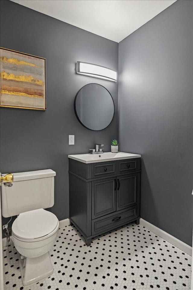 half bathroom with vanity, toilet, and baseboards