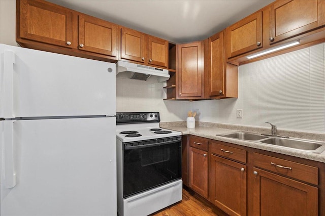 kitchen featuring brown cabinets, electric range oven, freestanding refrigerator, a sink, and under cabinet range hood