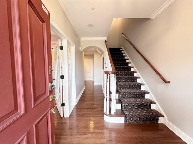 foyer featuring arched walkways, wood finished floors, baseboards, ornamental molding, and stairway