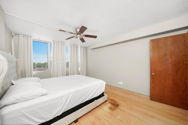 bedroom with ceiling fan, a textured ceiling, and wood finished floors