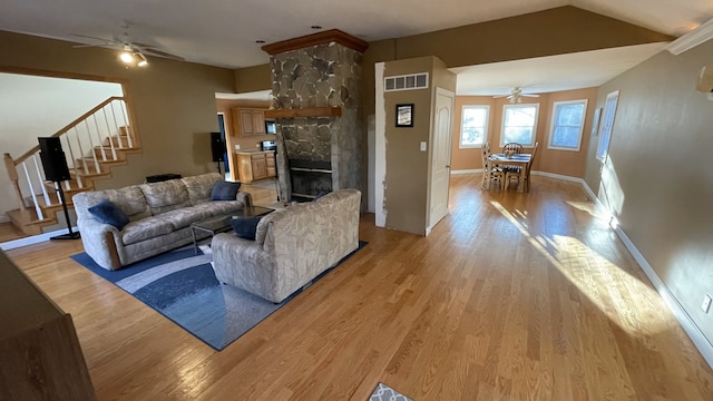 living area featuring light wood finished floors, visible vents, lofted ceiling, stairway, and a stone fireplace