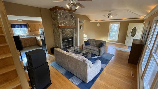 living room with lofted ceiling, light wood-style flooring, visible vents, and a stone fireplace