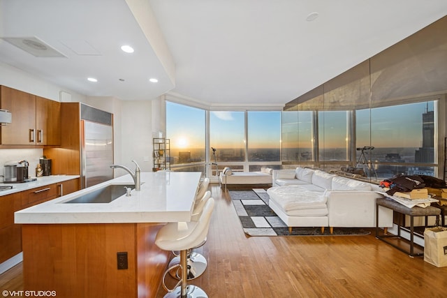 kitchen featuring light countertops, brown cabinetry, a sink, wood finished floors, and stainless steel built in refrigerator