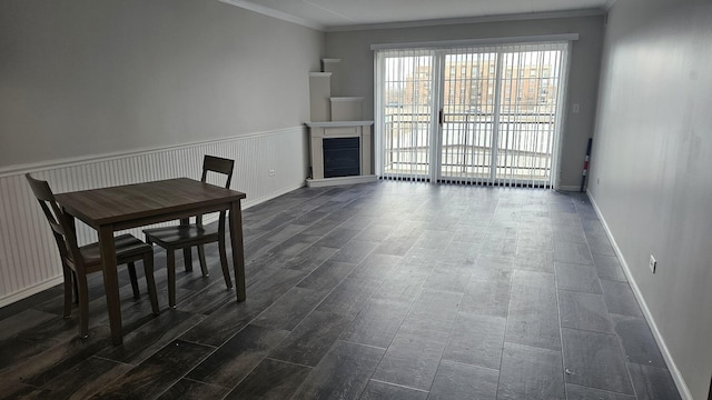 unfurnished dining area with baseboards, ornamental molding, a fireplace with raised hearth, and wainscoting