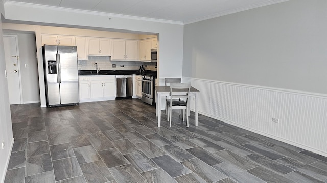 kitchen featuring stainless steel appliances, a sink, white cabinetry, wainscoting, and dark countertops