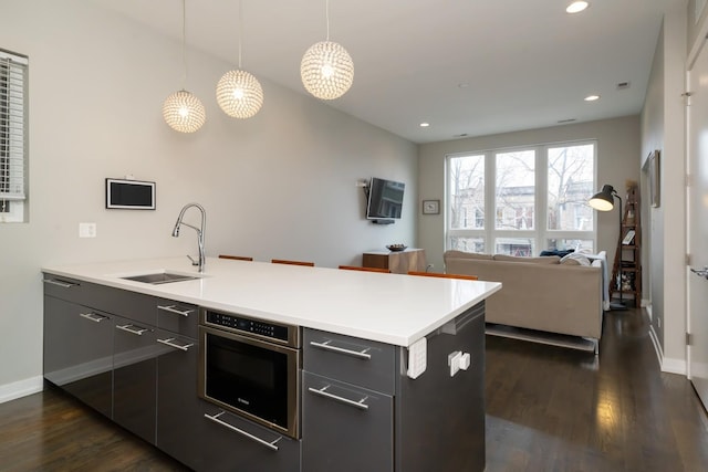 kitchen with dark wood-style floors, a peninsula, a sink, and light countertops