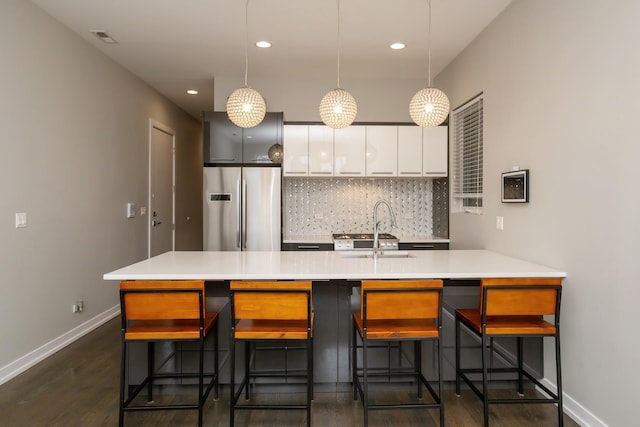 kitchen with a sink, visible vents, baseboards, stainless steel refrigerator, and tasteful backsplash