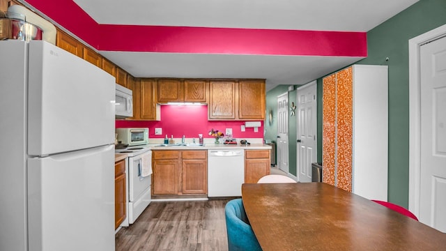 kitchen featuring brown cabinets, light countertops, a sink, wood finished floors, and white appliances