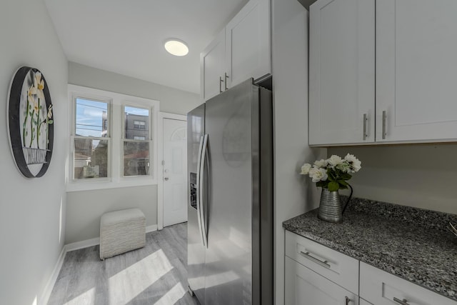 kitchen with dark stone counters, white cabinets, light wood-type flooring, stainless steel fridge, and baseboards