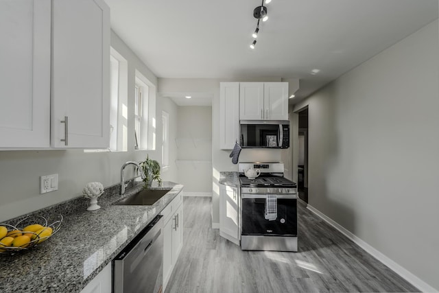 kitchen with stone countertops, white cabinets, light wood-style flooring, appliances with stainless steel finishes, and a sink