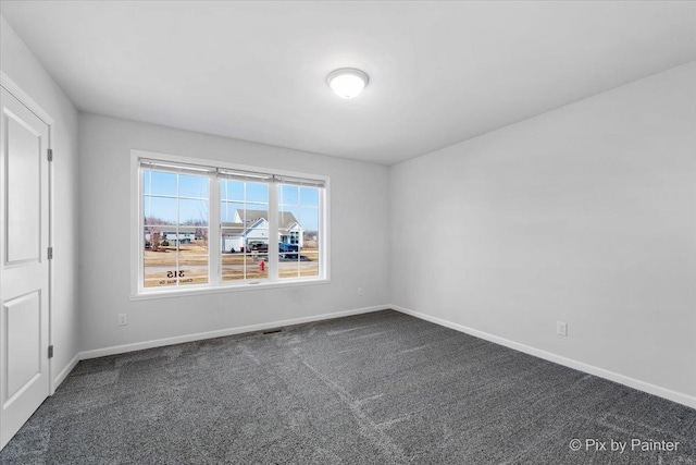 spare room featuring dark colored carpet and baseboards