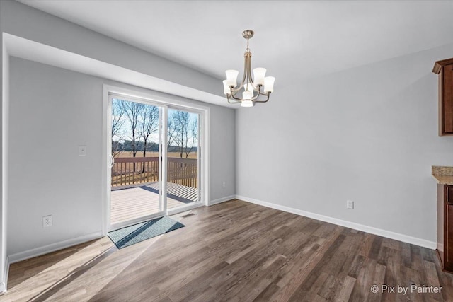 unfurnished dining area featuring a notable chandelier, dark wood finished floors, and baseboards