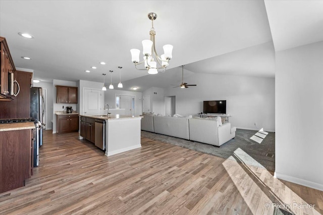 kitchen featuring stainless steel appliances, a sink, open floor plan, vaulted ceiling, and light countertops