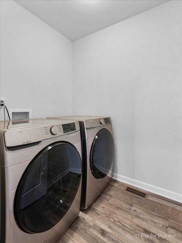 laundry room featuring visible vents, washing machine and dryer, wood finished floors, laundry area, and baseboards