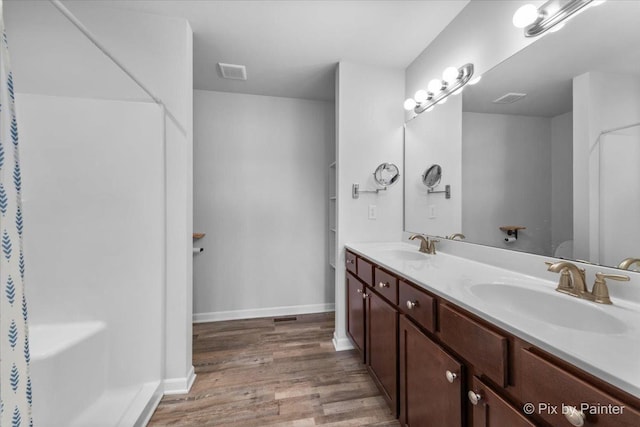 full bath featuring wood finished floors, a sink, visible vents, baseboards, and double vanity