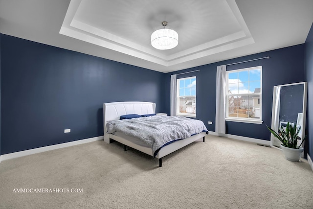 carpeted bedroom featuring a tray ceiling, a notable chandelier, and baseboards